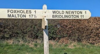 A wooden signpost with directions to Foxholes (1 mile), Malton (17.5 miles), Wold Newton (1 mile) and Bridlington (11 miles)