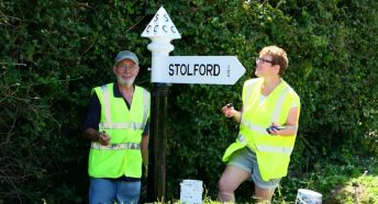 Two volunteers stand next to a newly painted fingerpost
