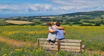 2 kids on bench in summer meadow enjoying the view