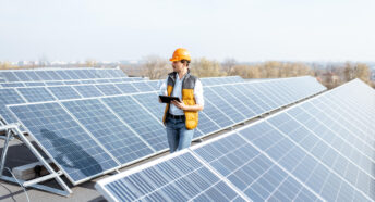 View on the rooftop solar power plant with mann walking and examining photovoltaic panels.
